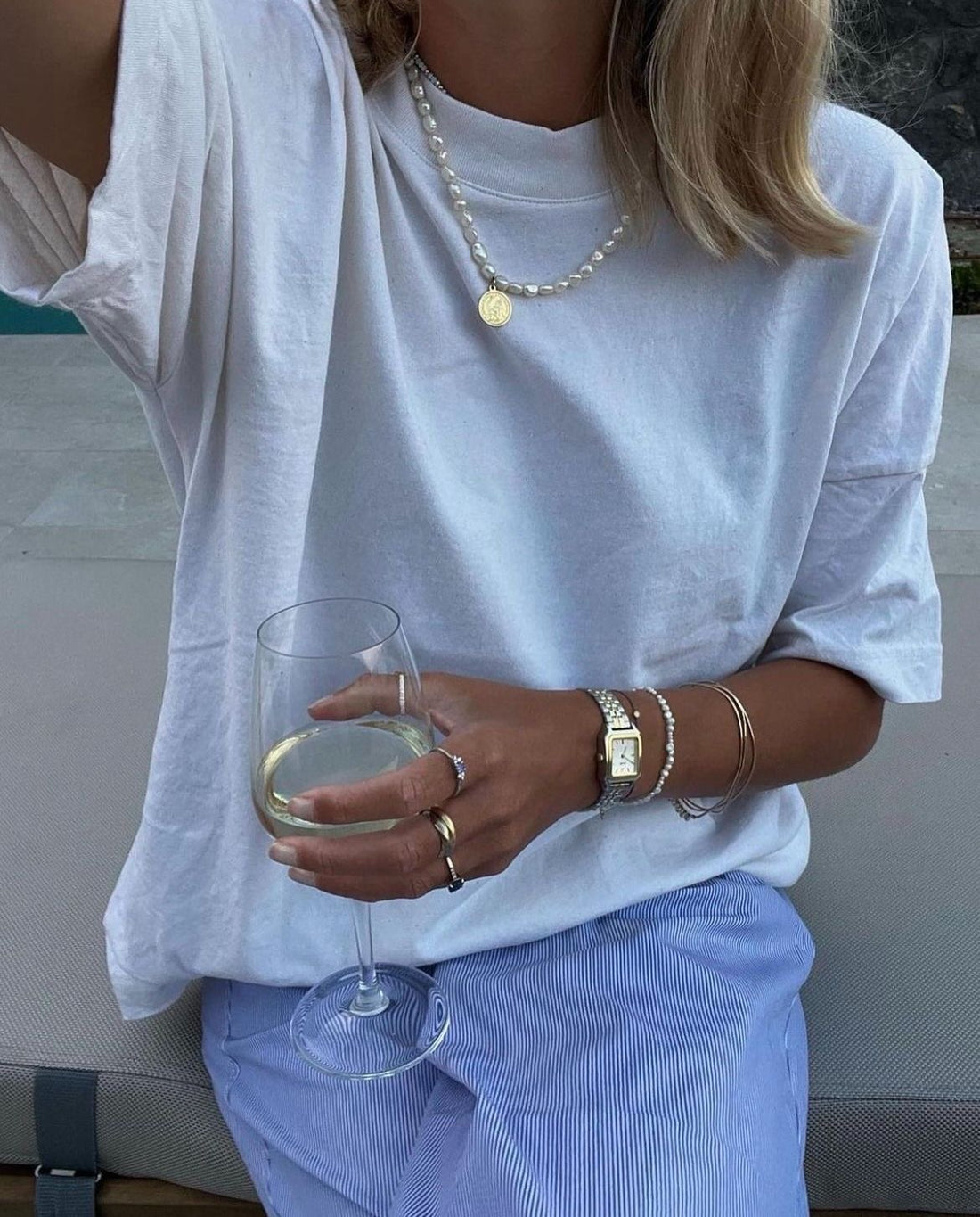 A woman wearing a lot of minimalist jewellery holding a glass of wine