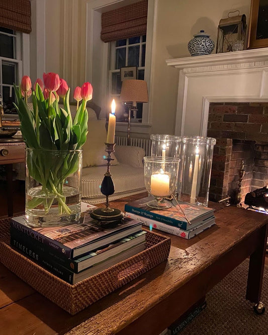 Photo of a coffee table with ambient candlelight, books, and tulips in a vase